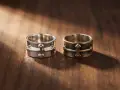 Dwa pierścionki z krzyżem na drewnianym tle. Jeden błyszczący, drugi ciemniejszy, jak próba 835 złoto czy srebro.