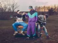 Trzech mężczyzn w dresach i swetrach, charakterystyczna moda lat 90. Siedzą na masce starego samochodu.