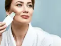 Kobieta w białym szlafroku wykonuje peeling kawitacyjny w domu, poprawiając wygląd swojej skóry.