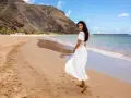 Kobieta w zwiewnej białej sukience spaceruje po plaży, prezentując idealne stylizacje nad morze.