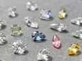 Różne rodzaje diamentów: białe, zielony, niebieski, różowy i żółty, o rozmaitych szlifach, błyszczą na szarym tle.