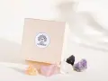 Drewniane pudełko z logo "BASIC CRYSTALBOX" i pięcioma surowymi kamieniami: pomarańczowym, różowym, białym, czarnym i fioletowym. Idealne, by dowiedzieć się, jak wybrać swój kamień.