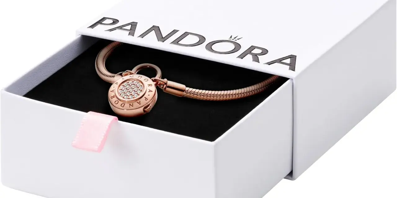 Elegancka bransoletka Pandora z charmsami w kolorze różowego złota, ozdobiona cyrkoniami, w białym pudełku z różową wstążką.