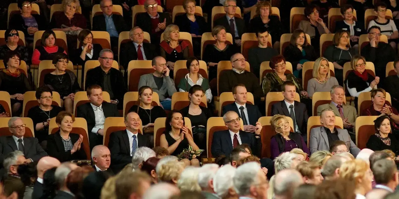 Elegancko ubrani ludzie siedzą w filharmonii, gotowi na koncert. Dowiedz się, jak ubrać się do filharmonii, by wyglądać stylowo.