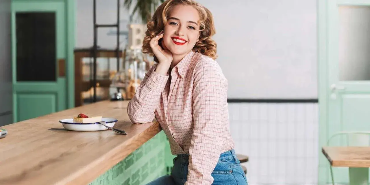 Uśmiechnięta blondynka w koszuli w kratę i dżinsach, stylizacja inspirowana modą PRL lat 70.