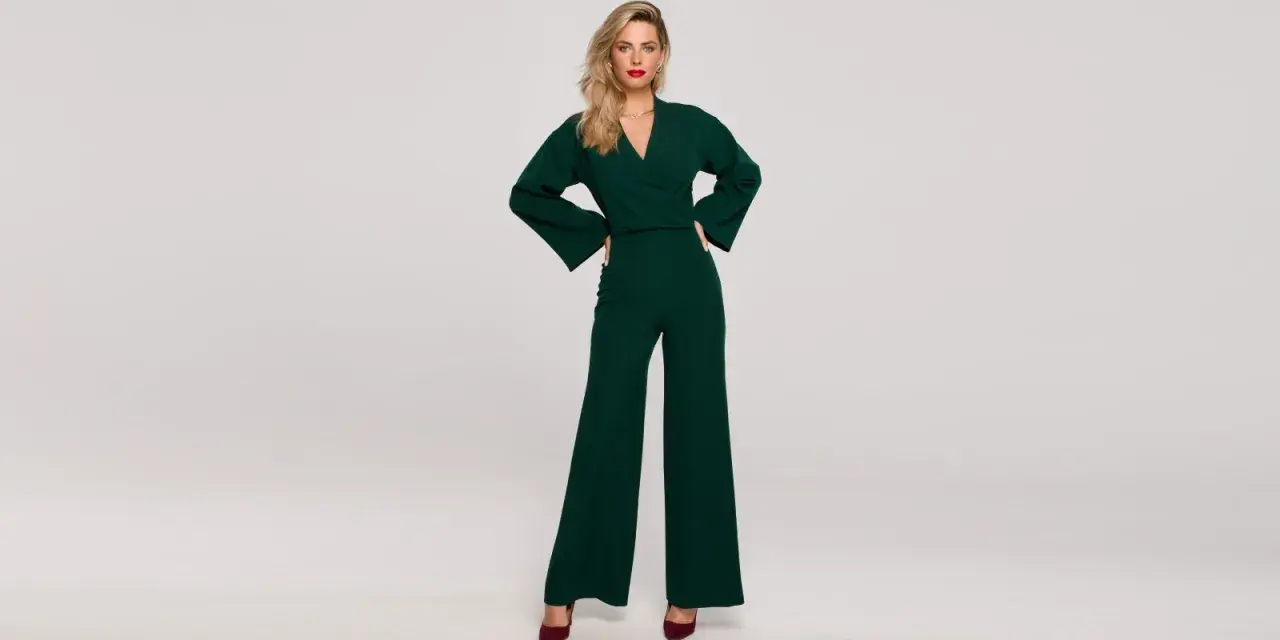 Elegancka kobieta w zielonym kombinezonie z szerokimi nogawkami. Góra kombinezonu ma dekolt kopertowy i szerokie rękawy.