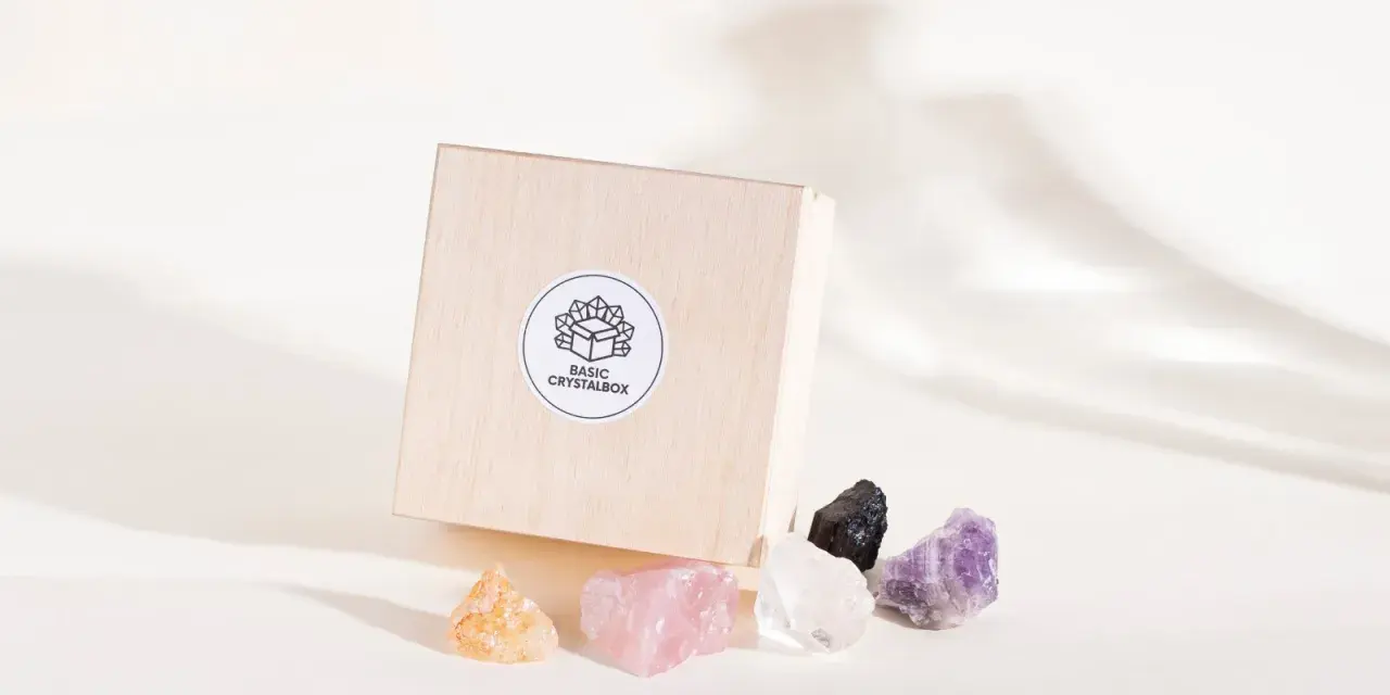 Drewniane pudełko z logo "BASIC CRYSTALBOX" i pięcioma surowymi kamieniami: pomarańczowym, różowym, białym, czarnym i fioletowym. Idealne, by dowiedzieć się, jak wybrać swój kamień.