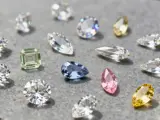Różne rodzaje diamentów: białe, zielony, niebieski, różowy i żółty, o rozmaitych szlifach, błyszczą na szarym tle.
