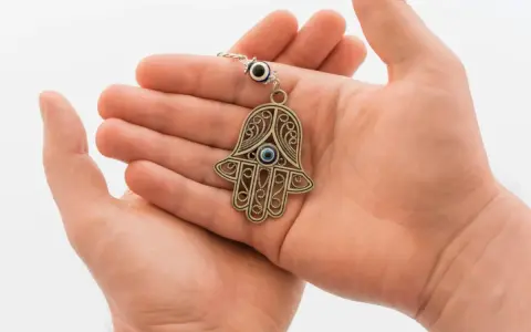 Otwarta dłoń trzyma wisiorek w kształcie dłoni Fatimy, symbol ręka opatrzności, chroniący przed złym okiem.