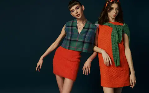 Dwie modelki w stylizacjach inspirowanych modą lat 60. Jedna w kraciastej kamizelce i pomarańczowej spódniczce, druga w pomarańczowej sukience i zielonym sweterku.