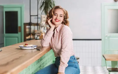 Uśmiechnięta blondynka w koszuli w kratę i dżinsach, stylizacja inspirowana modą PRL lat 70.