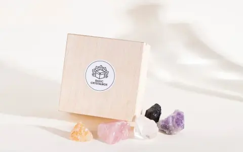 Drewniane pudełko z logo "BASIC CRYSTALBOX" i pięcioma surowymi kamieniami: pomarańczowym, różowym, białym, czarnym i fioletowym. Idealne, by dowiedzieć się, jak wybrać swój kamień.
