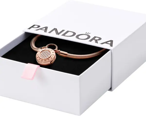 Elegancka bransoletka Pandora z charmsami w kolorze różowego złota, ozdobiona cyrkoniami, w białym pudełku z różową wstążką.