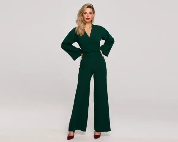 Elegancka kobieta w zielonym kombinezonie z szerokimi nogawkami. Góra kombinezonu ma dekolt kopertowy i szerokie rękawy.