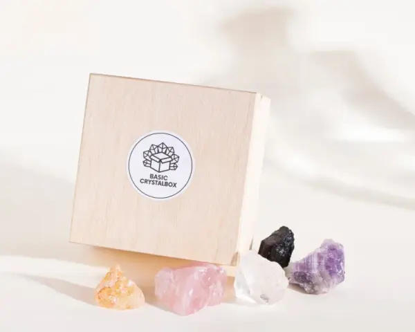 Drewniane pudełko z logo "BASIC CRYSTALBOX" i pięcioma surowymi kamieniami: pomarańczowym, różowym, białym, czarnym i fioletowym. Idealne, by dowiedzieć się, jak wybrać swój kamień.