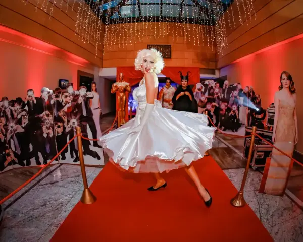 Impreza w stylu Hollywood: postać Marilyn Monroe na czerwonym dywanie, otoczona paparazzi i gwiazdami. Idealna inspiracja, jak się ubrać na galę!