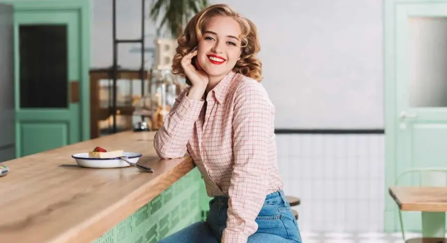 Uśmiechnięta blondynka w koszuli w kratę i dżinsach, stylizacja inspirowana modą PRL lat 70.