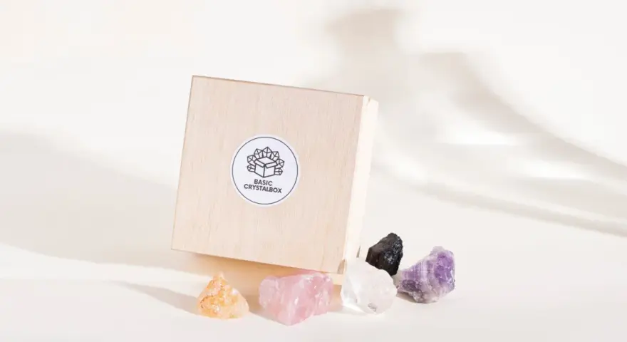 Drewniane pudełko z logo "BASIC CRYSTALBOX" i pięcioma surowymi kamieniami: pomarańczowym, różowym, białym, czarnym i fioletowym. Idealne, by dowiedzieć się, jak wybrać swój kamień.