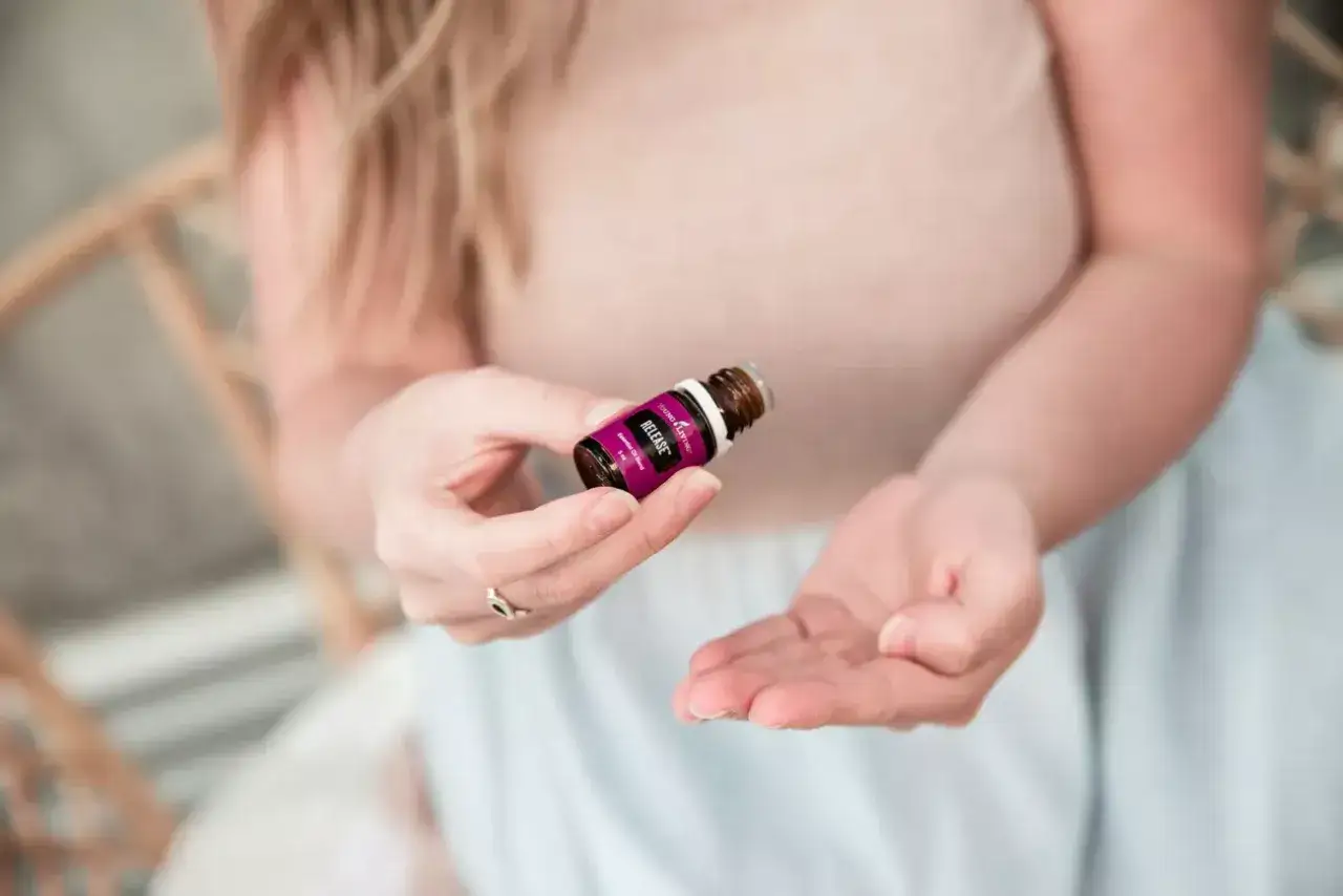 Kobieta trzyma buteleczkę olejku eterycznego, przygotowując się do aromaterapii. To prosty spos&oacute;b na relaks i odprężenie.